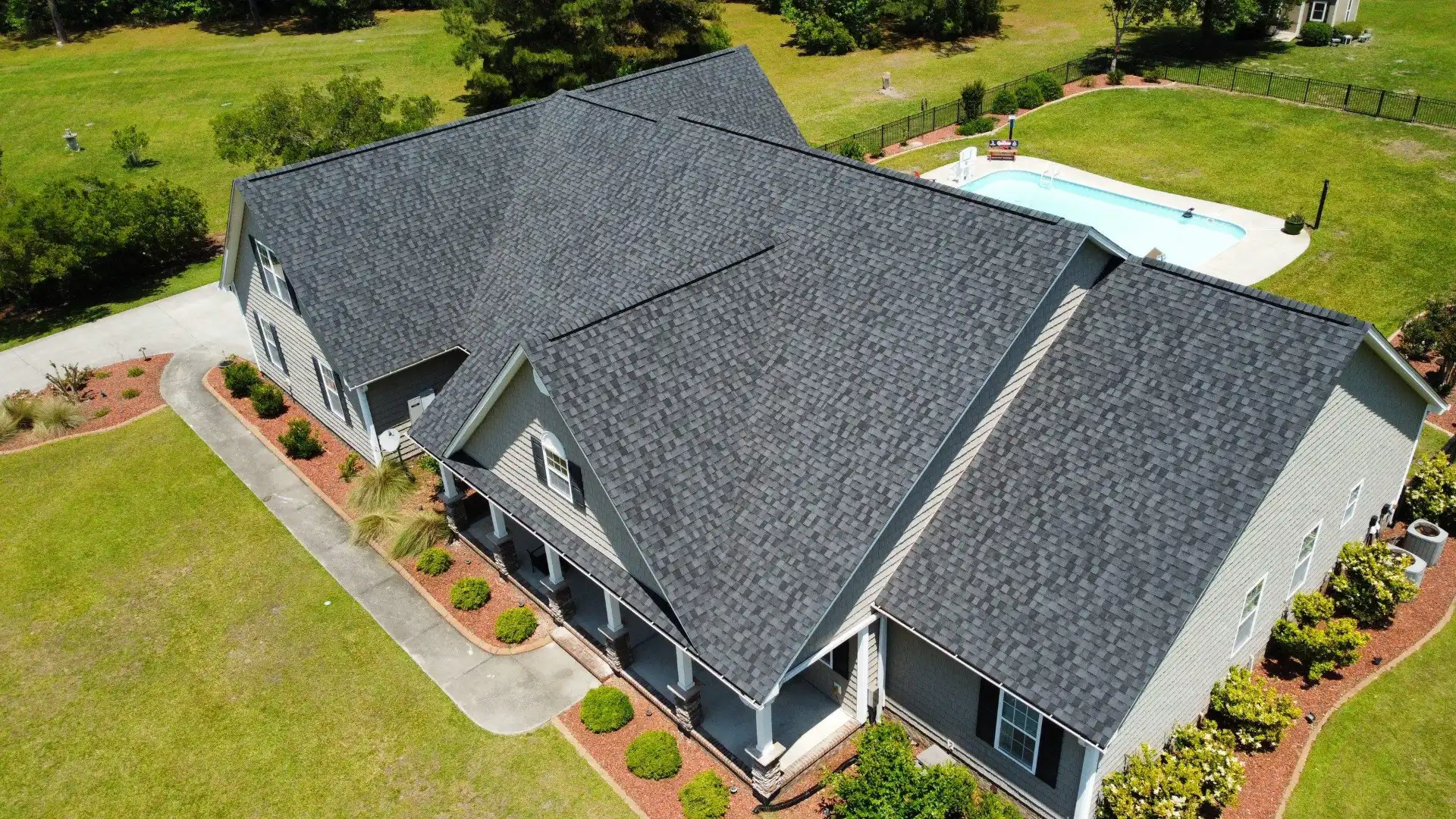 A new gray architectural shingle roof on a large house with a pool, seen from a drone