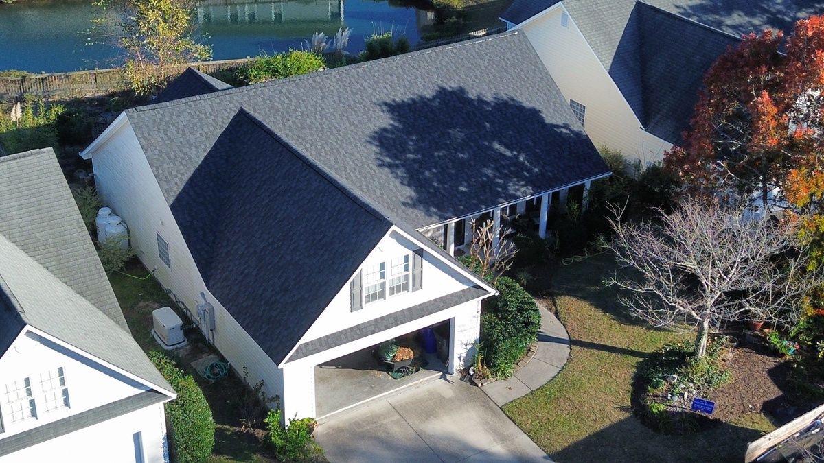 A new gray shingle roof on a white house with a two-car garage, seen from a drone