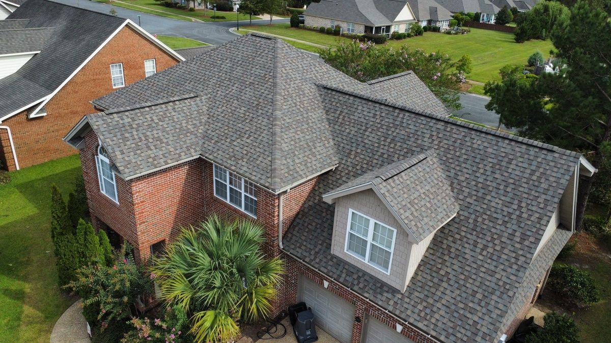 A new shingle roof on a brick house with dormers, seen from a drone