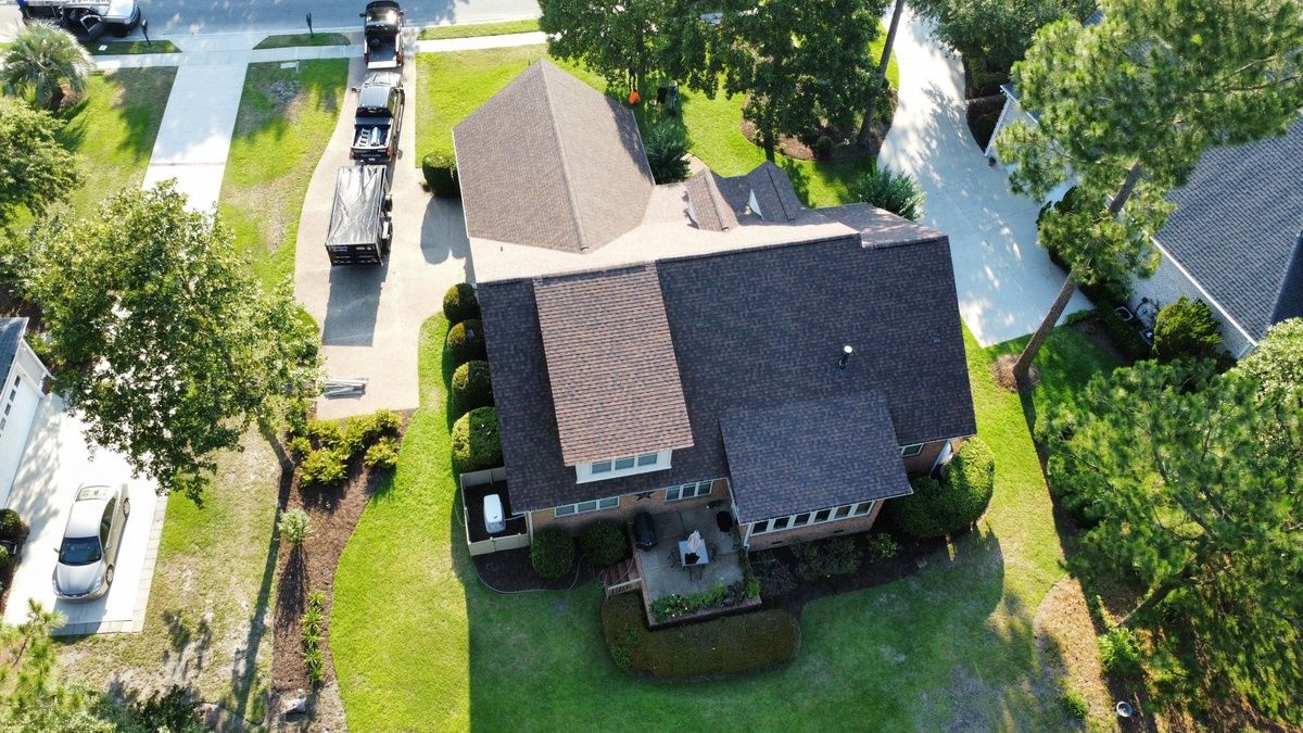 A new shingle roof on a house among tall pines, seen from a drone