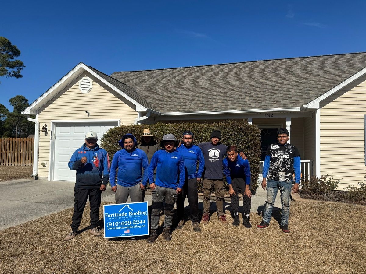 The Fortitude Roofing crew in blue company shirts in front of a finished house, with a Fortitude yard sign