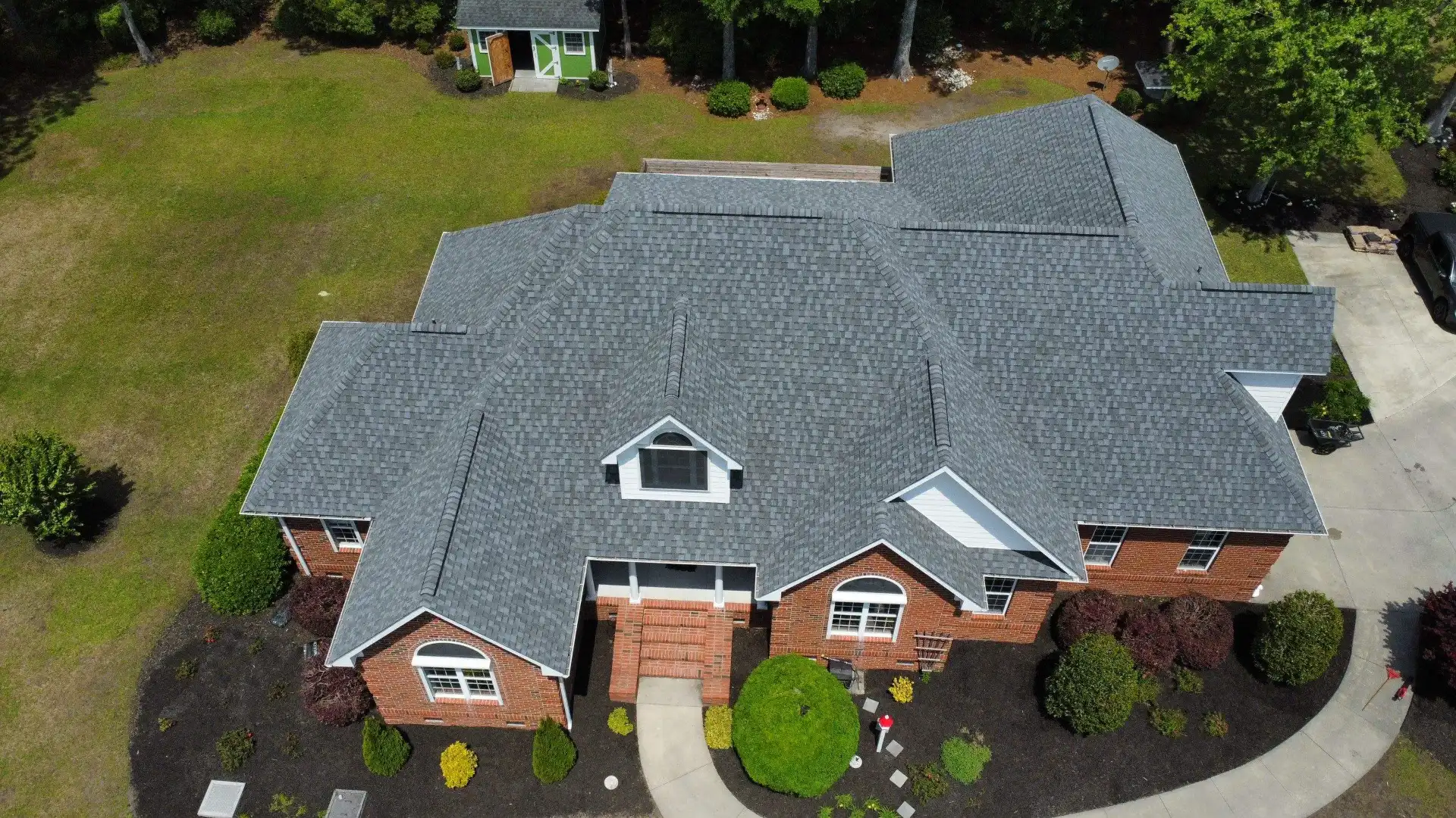 A new gray shingle roof on a large two-story house with a side-load garage, seen from a drone