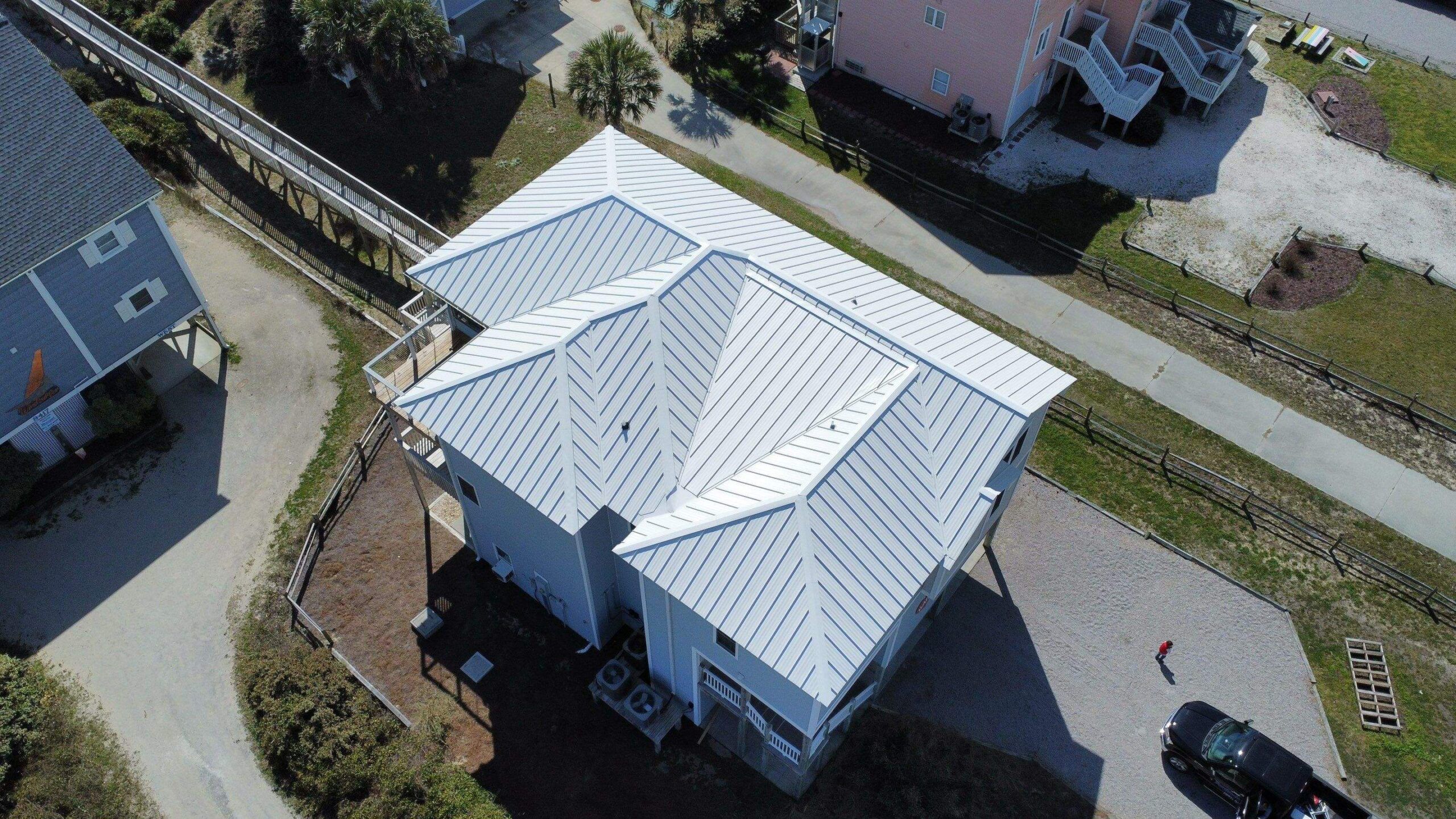 A new white standing seam metal hip roof on a raised coastal house, seen from a drone