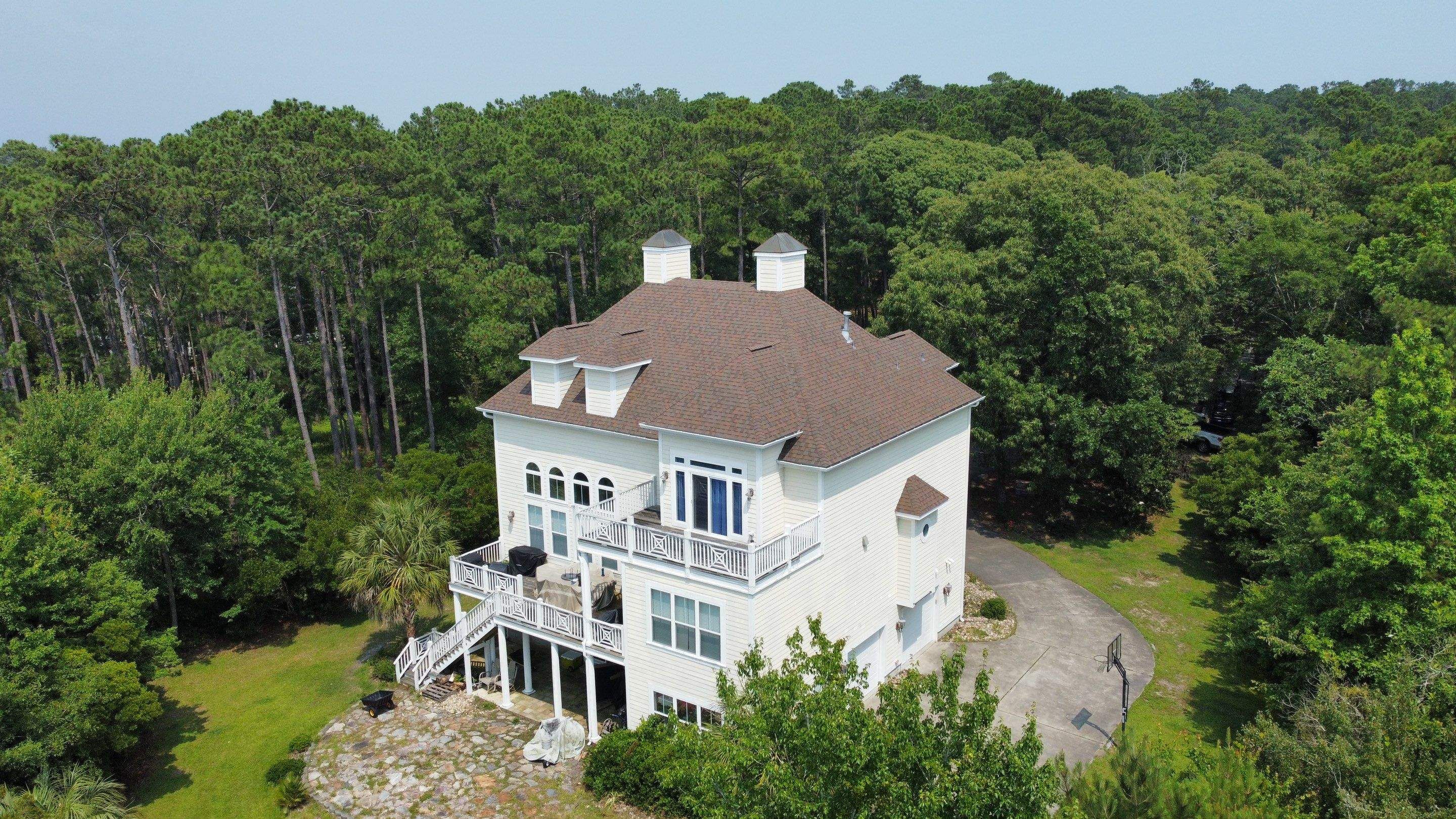 A new brown shingle roof on a white three-story house in the woods, seen from a drone