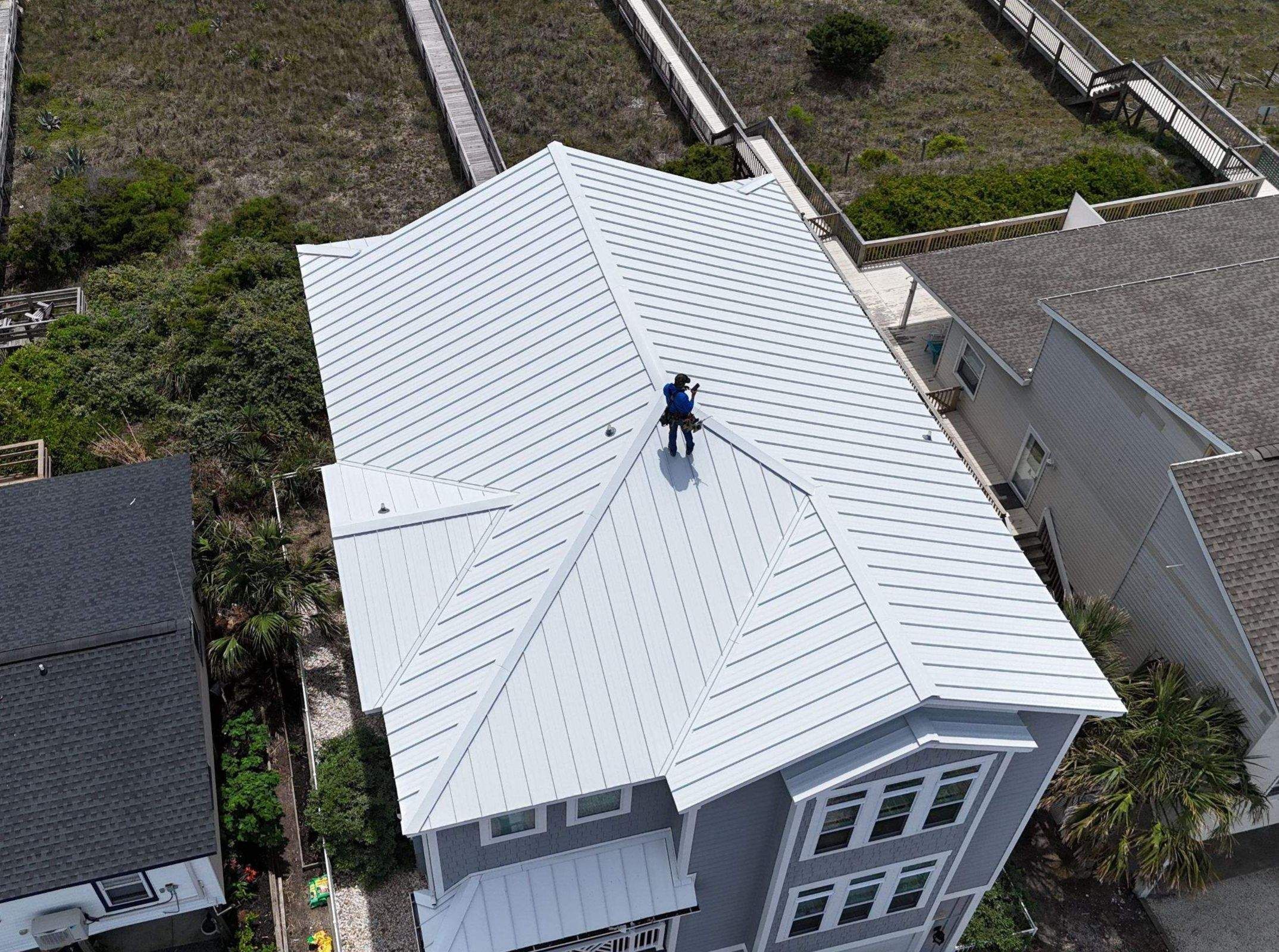 A Fortitude roofer on a new white standing seam metal roof on a beach house, seen from a drone