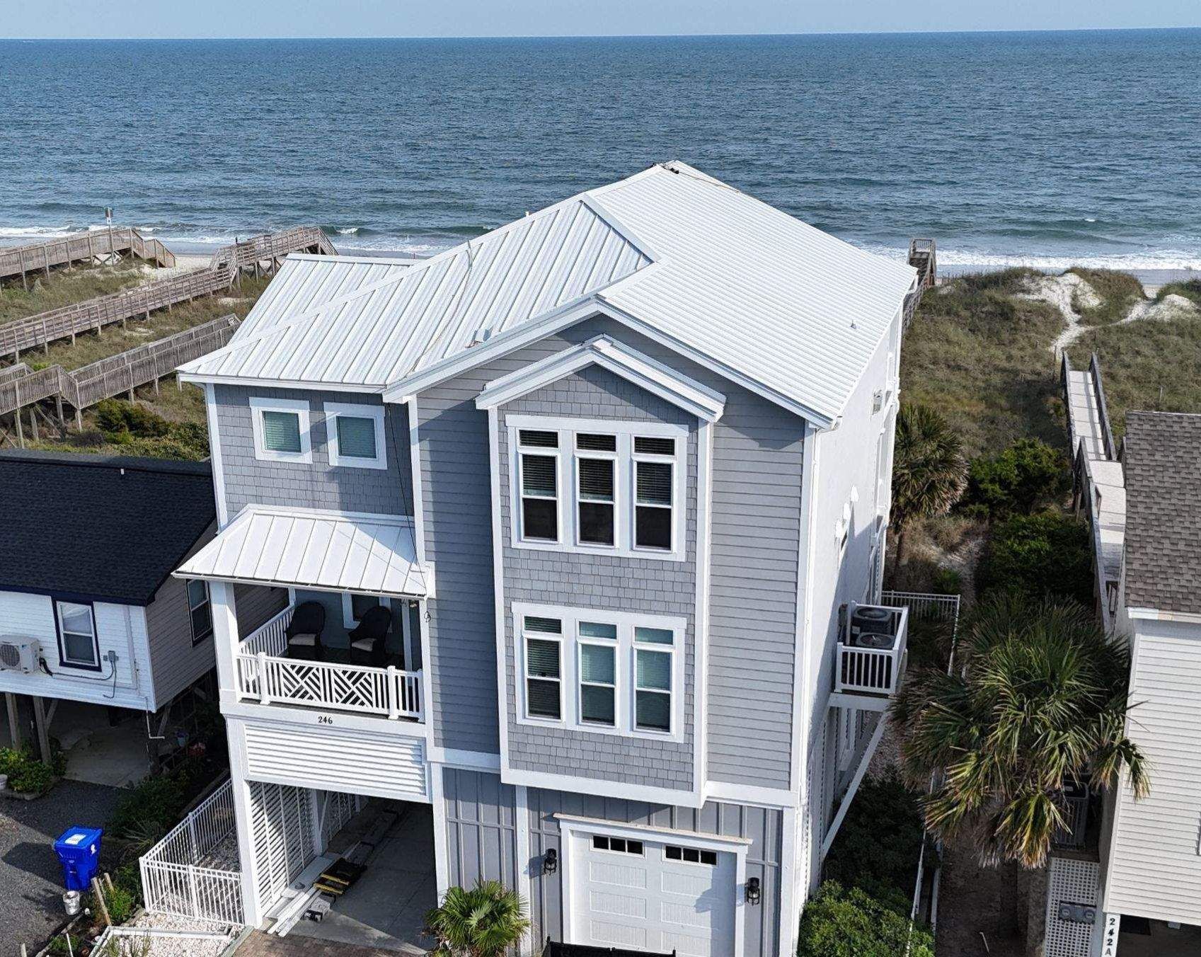 A new white standing seam metal roof on a gray three-story beach house, with the dunes and the ocean behind it