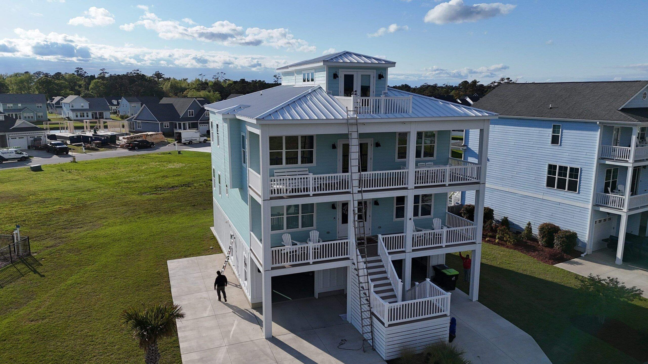 A mint-green raised beach house with wraparound porches and a new white standing seam metal roof
