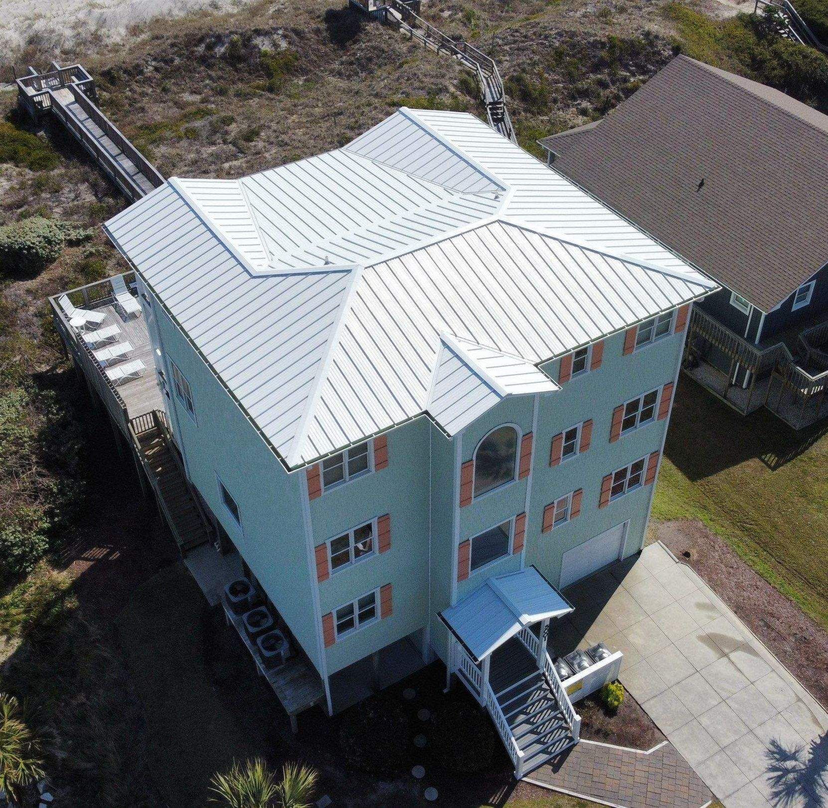 A new white standing seam metal roof on a pale green coastal house with orange shutters, seen from a drone