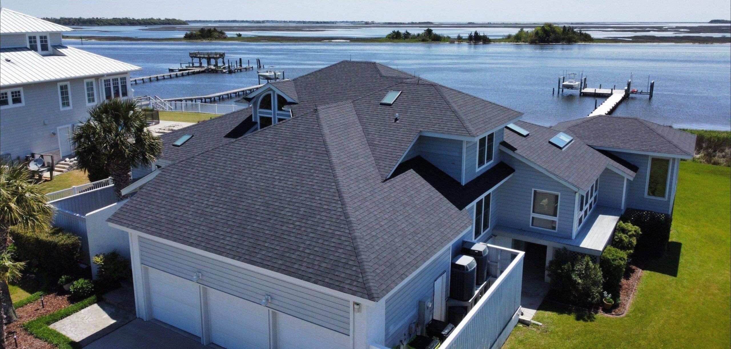 A new gray shingle roof on a large house with a three-car garage, with the water behind it