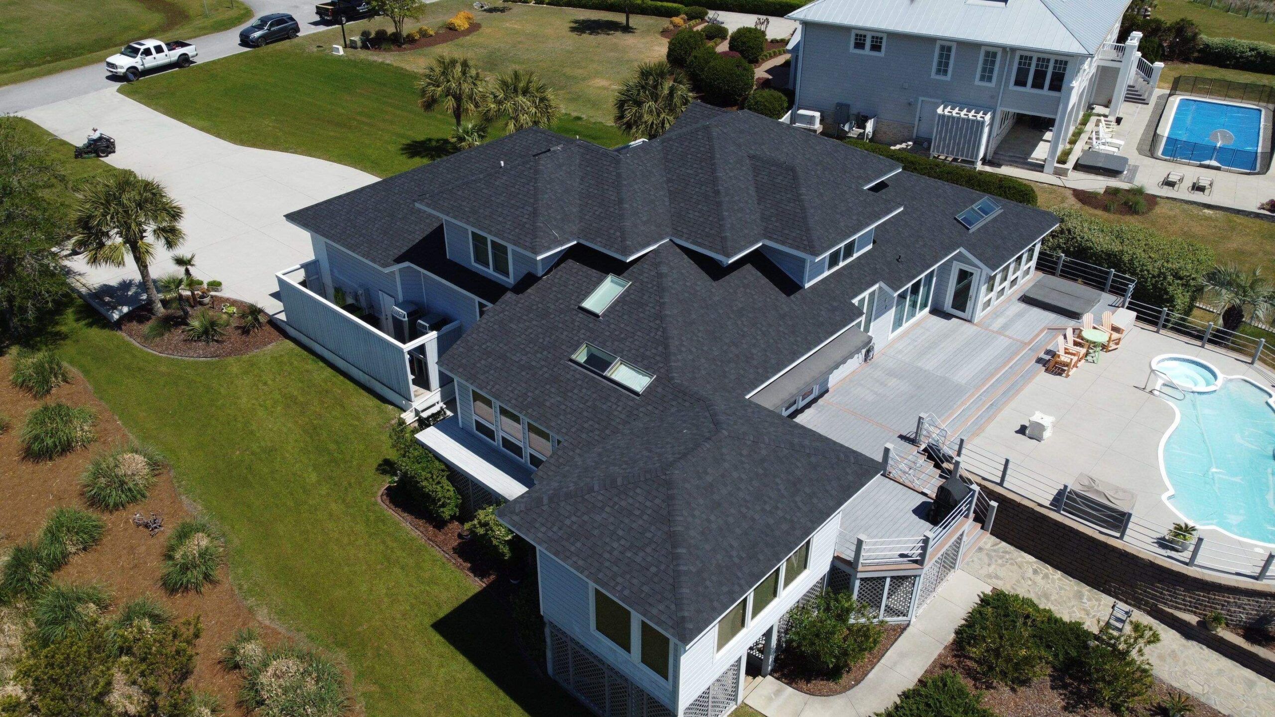 A new gray shingle roof on a waterfront house with a pool, seen from a drone