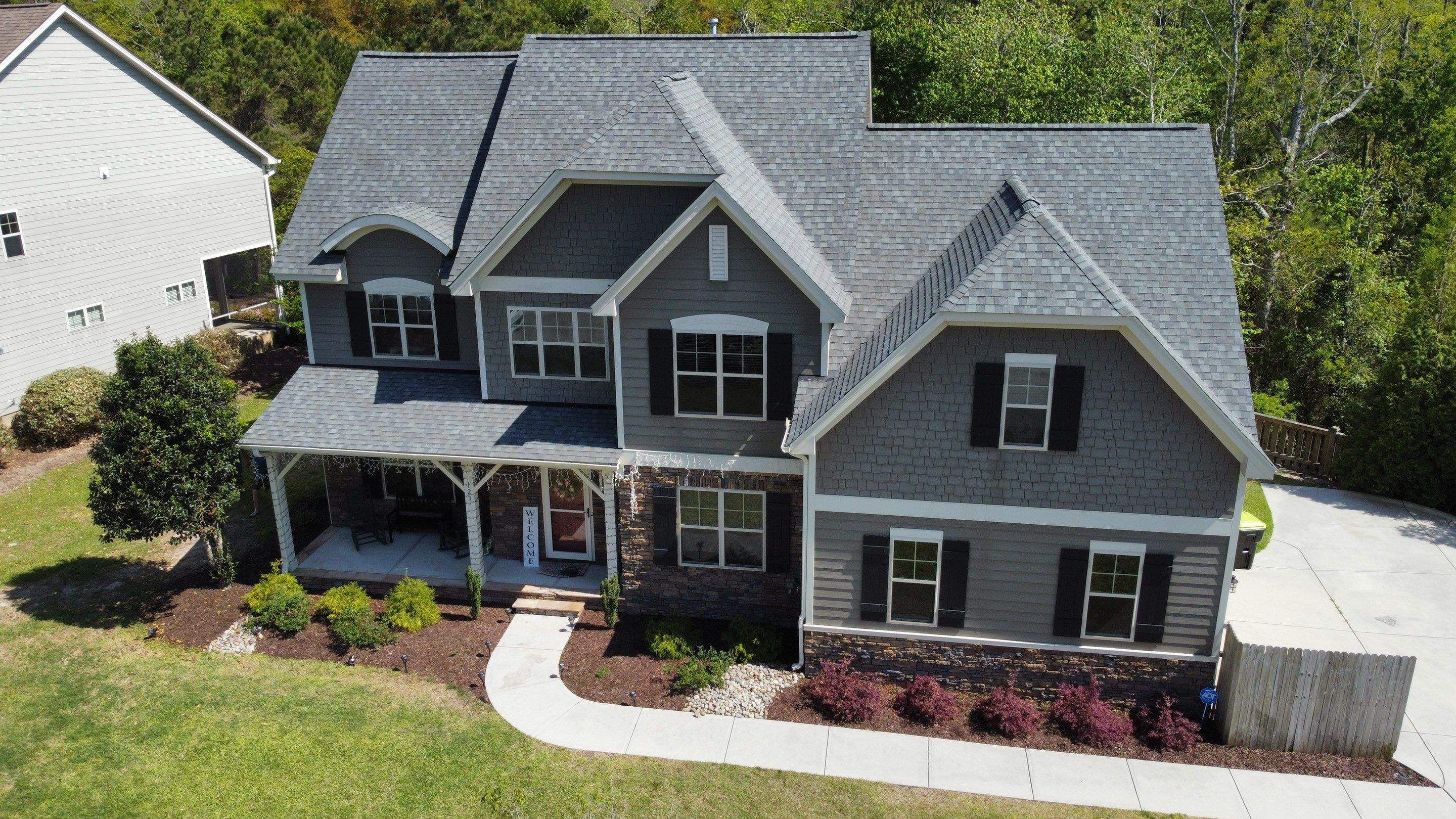 A new shingle roof on a gray two-story house with a stone front and a long front walk