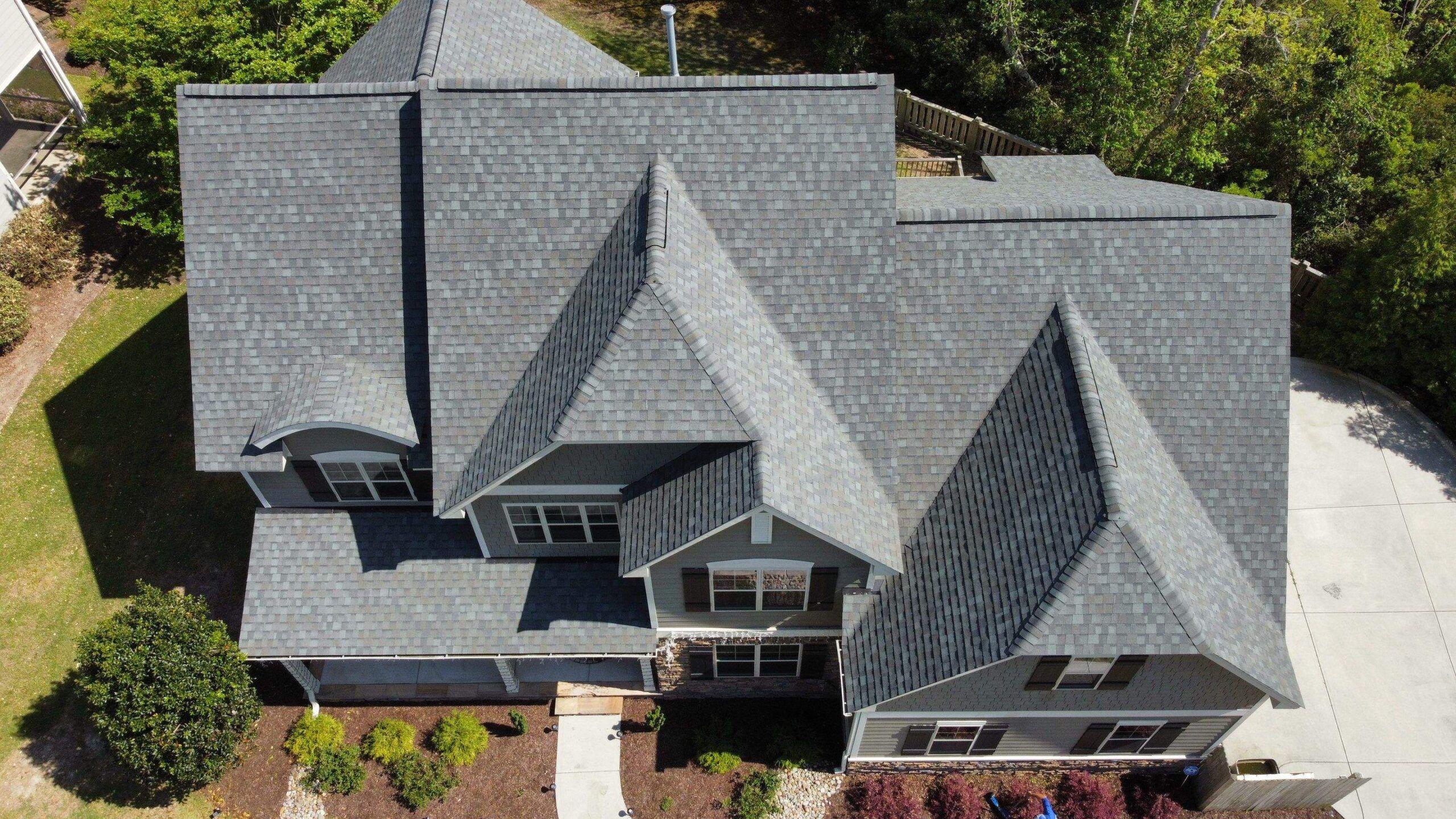 A new gray shingle roof with several gables, seen straight down from a drone
